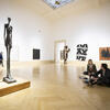 Two students sitting on the floor of a museum in front of Giacommetti sculpture